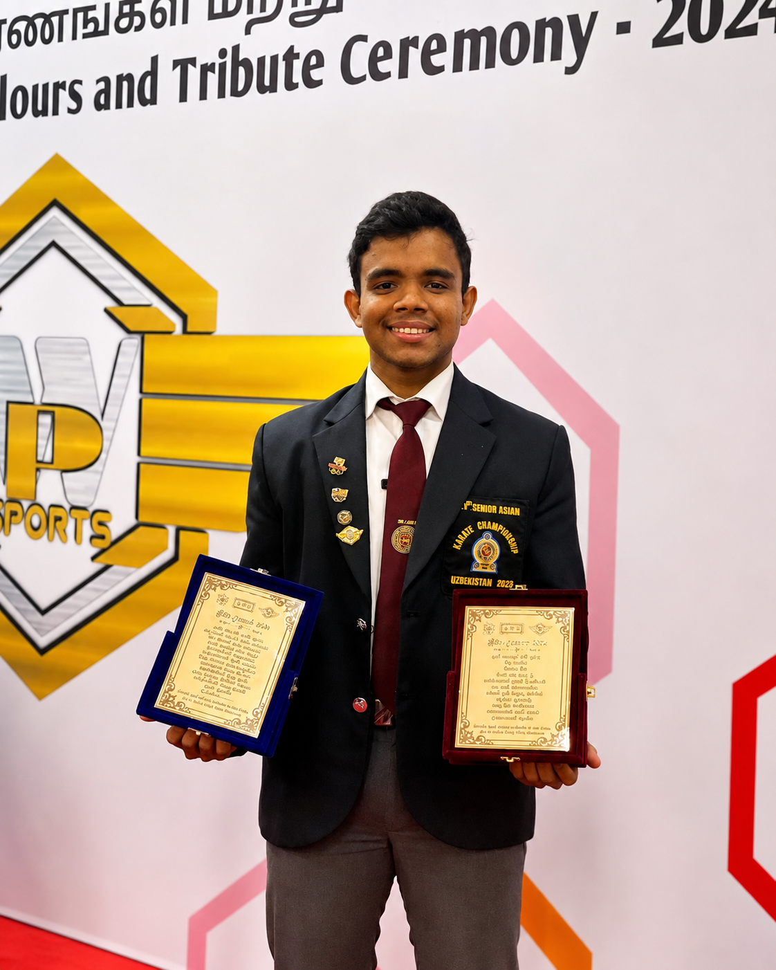 Karate champion holding two commemorative award plaques at an honours ceremony