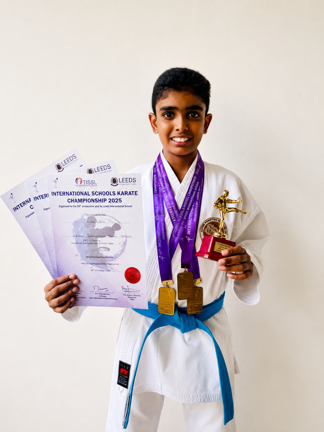 Young karate athlete with three medals, certificates and a trophy from the International Schools Karate Championship 2025
